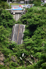 A collapsed road bridge surrounded by dense green vegetation (Sugaru Kuzure), Japan. Broken metal...
