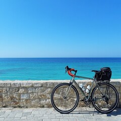 Fototapeta premium A sleek bicycle with red handlebars rests against a stone wall, overlooking a stunning blue ocean on a sunny day.