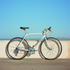 Obraz premium A classic light blue bicycle parked against a seaside wall, with clear skies and calm ocean waves in the background.