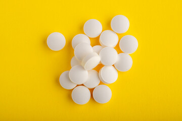 White round pills isolated on a yellow background. A heap of small round meds. Health care and medicine concept