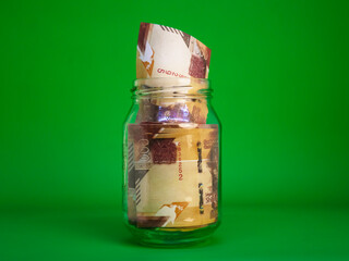 Kenyan Shilling notes in transparent glass jar bottle container isolated green background. savings...