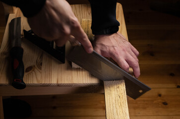 Close-up of a carpenter's hands using a hand saw to carefully cut a wooden plank on a workbench, emphasizing precision and craftsmanship