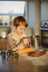 Cozy morning: a child in festive pajamas baking gingerbread cookies in a sunny kitchen.