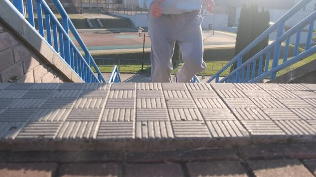 Man in light blue hoodie climbs outdoor steps with blue railings. Active workout, fitness training