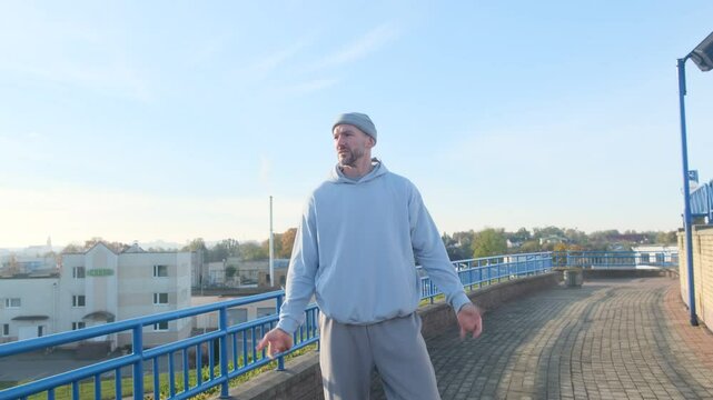 Athlete warming up outdoors, wearing a light blue hoodie, with a city background. Fitness and healthy lifestyle concept