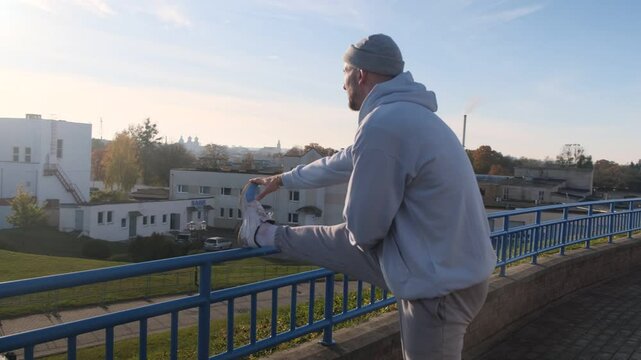 Person stretching leg on blue railing outdoors, with urban background. Warm-up and fitness concept