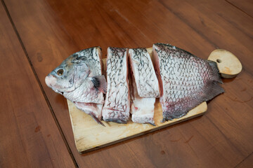 Close-up view of raw pieces of giant gourami fish on a wooden chopping board in kitchen table, preparation for cooking