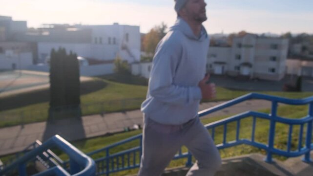 Focused athlete runs up outdoor stairs with blue railings. Workout and training in an urban setting