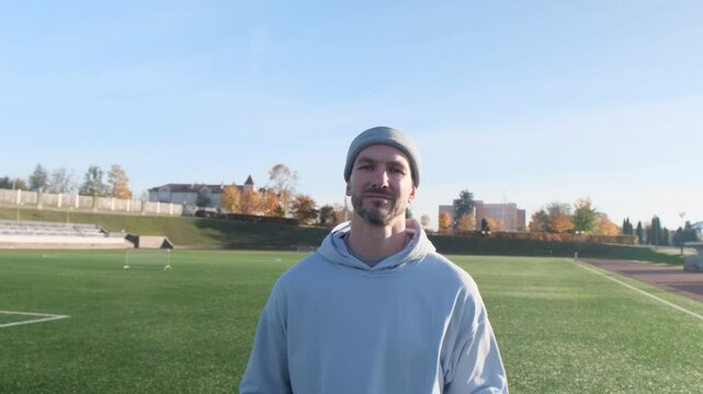 Football player doing hand-to-hand ball tosses. Man in a gray beanie on a soccer field. Sunny day, autumn scenery