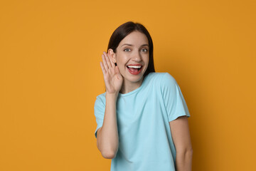 Woman showing hand to ear gesture on orange background