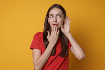 Woman showing hand to ear gesture on orange background