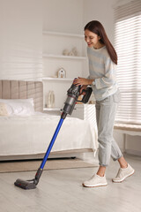 Young woman cleaning floor with cordless vacuum cleaner in bedroom