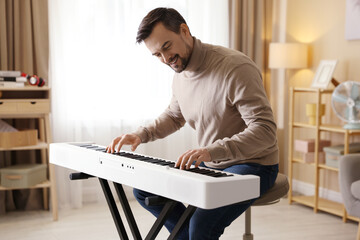 Smiling man playing synthesizer at home. Electronic musical instrument