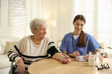 Caregiver measuring patient's blood pressure at table indoors. Home health care service