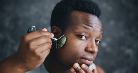 Man, jade roller and skincare in home for grooming, wellness or stone for massage in morning. African person, tools and facial treatment with process, cosmetics or transformation in bathroom at house