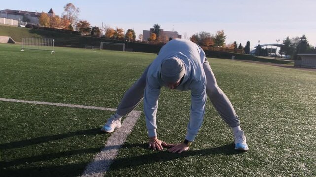 Footballer warming up on the field, dressed in a hoodie and sweatpants. He is preparing for training