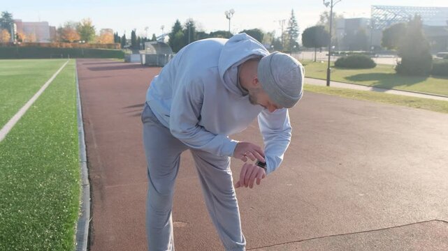 Man leaning over after run at soccer field. Grey hat, grey sweatshirt, grey pants. Sport, tired, exhausted