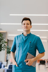 Young doctor holding a tablet and looking at the camera in a modern clinic.