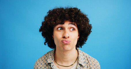 Man, face and pout with afro for kiss, flirty expression or dream in fashion on a blue studio background. Male person, gen z or awkward model with curly hair, funny attitude or emoji lips on space