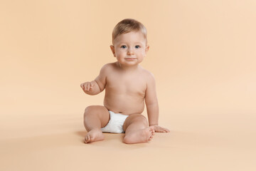 Cute little baby in diaper sitting on beige background