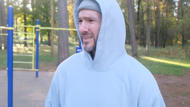 Man in hoodie warms up outdoors before workout. Focus on his face, determination, athlete prepares