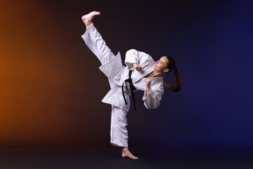 Young woman in kimono practicing karate on dark background