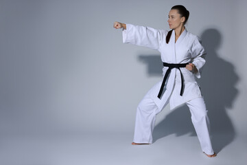 Young woman in kimono practicing karate on grey background, space for text