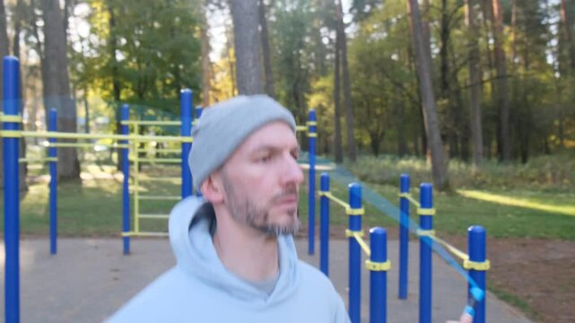 An athlete does skipping rope in the open air. A man in a hoodie is actively exercising in nature. Dynamic movements