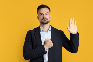 Man making promise with raised hand on orange background. Oath gesture