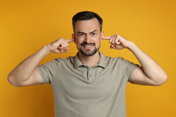 Fototapeta premium Man covering his ears with fingers on orange background