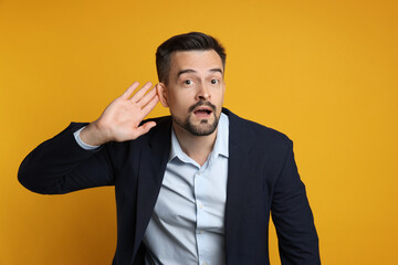 Man showing hand to ear gesture on orange background