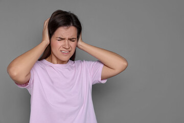 Woman covering her ears on grey background, space for text