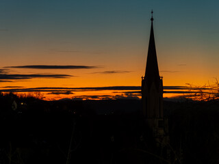 Obraz premium Golden sunset silhouetting a church spire against a colorful sky in the evening hours