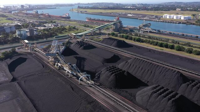 Aerial view of piles of coal, coal conveyors, and bulk carriers moored on the Hunter River waiting to be loaded with coal in the Port of Newcastle, NSW, Australia.