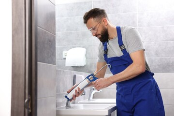 Worker with caulking gun sealing washbasin in bathroom