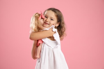 Cute little girl embracing her doll on pink background