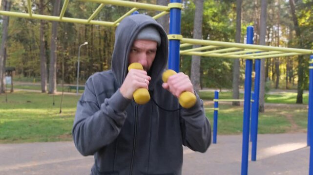 Man boxing with dumbbells outdoors in a park. Fitness, active lifestyle, strength training, healthy, workout concept