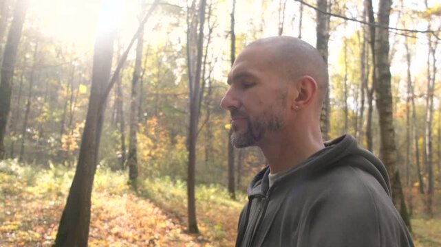 Profile of a man in a hooded sweatshirt walking through an autumn forest, bathed in sunlight