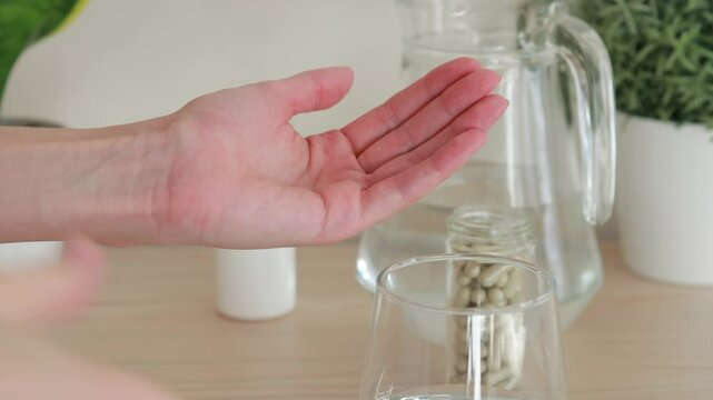 Close-up woman taking two gray pill capsules and drinking a glass of water