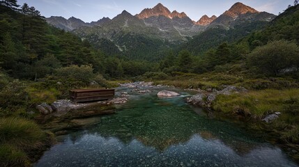 Tranquil mountain landscape with a clear stream and a serene forest setting beneath towering peaks at dawn.