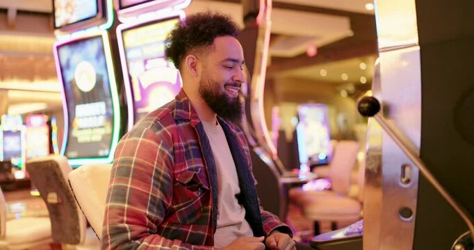 In a vibrant and lively casino atmosphere, filled with excitement and great possibilities, a young man joyfully celebrates a significant win at a slot machine, surrounded by cheering onlookers