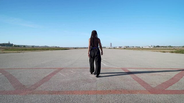Chica luchadora en artes marciales camina hacia el infinito en una pista de aterrizaje, como concepto de destino o del camino que hay que recorrer hacia el futuro.
