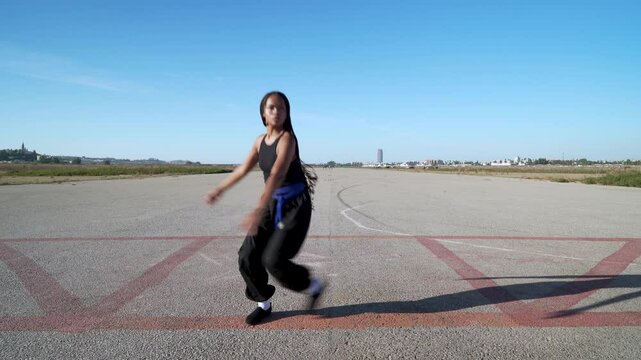 mujer joven bailando danza oriental en el paisaje infinito y minimalista de una pista de aterrizaje un d&iacute;a soleado con cielo azul como concepto de un buen viaje.
