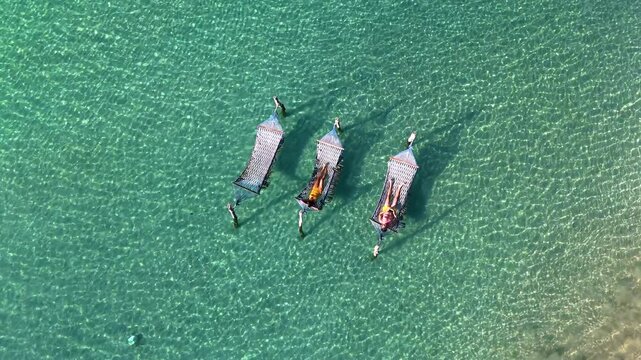 Discover the serene beauty of Koh Kood Island as sunbathers lounge in comfy hammocks surrounded by turquoise waters. A diverse couple of men and women on vacation in Thailand