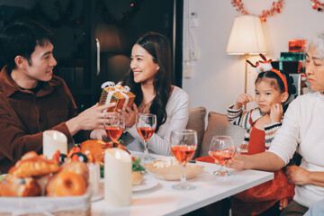 Portrait of Asian family exchanging presents during christmas at home. Attractive happy people holding gift box, celebrate holiday thanksgiving, xmas eve tradition in living room in house together.