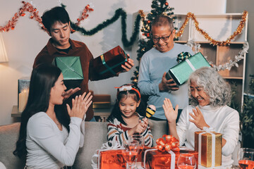 Portrait of Asian family exchanging presents during christmas at home. Attractive happy people holding gift box, celebrate holiday thanksgiving, xmas eve tradition in living room in house together.