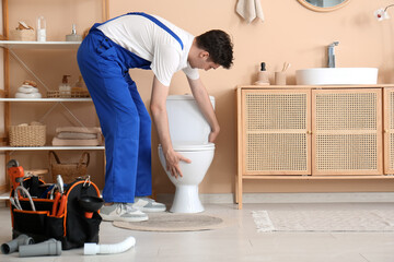 Male plumber with tool bag installing toilet in restroom