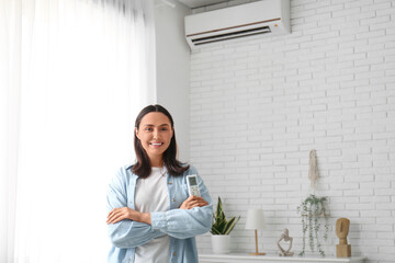 Pretty young woman with air conditioner remote control at home