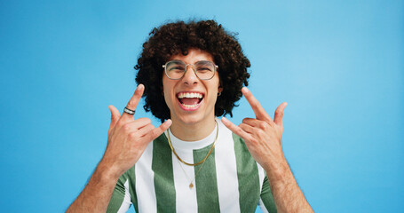 Portrait, rock on and hand gesture with man in studio on blue background with crazy, energy and shout. Rocker, hardcore and male person posing with devil horns, sign or symbol for concert freedom