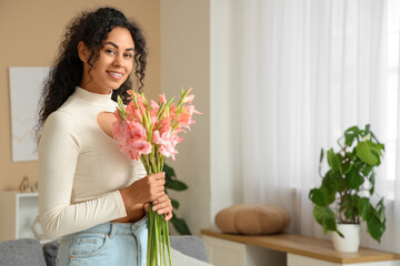 Beautiful young happy African-American woman with bouquet of pink gladiolus flowers at home